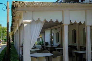 Beyaz ahşap boş restoran terasında beyaz masalar ve sandalyeler. Şehir caddesinde açık bir kafe. Kentsel yaşam tarzı