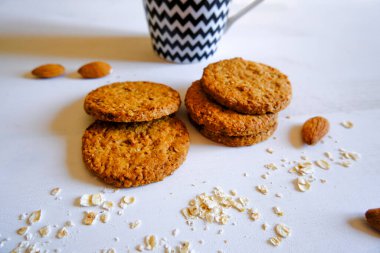  Yulaf ezmeli kurabiye, beyaz arka planda badem beyaz ve siyah çizgili kupa, kırıntılar. Sağlıklı yemek. Kahvaltı..