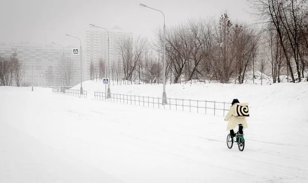 Der Kurier fährt mit dem Fahrrad durch eine verschneite Stadt. Das Konzept der Einsamkeit in einer Großstadt. — Stockfoto