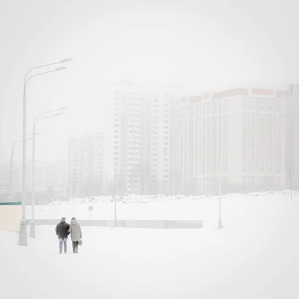 An adult couple walks through a snowy city. Loneliness in a big city.