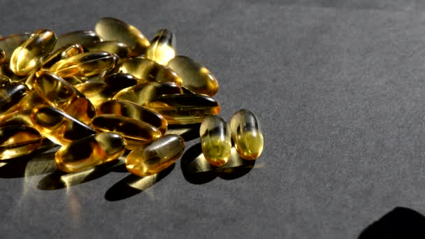 Omega 3 gold fish oil capsules pour on top, black background, macro — Stock Video