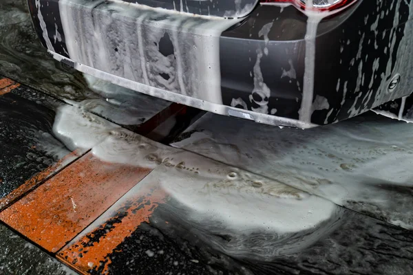 Auto v pěně u myčky. Špinavé auto po ošetření mýdlovou vodou. špinavá pěna — Stock fotografie
