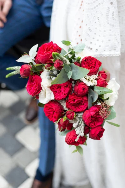 Κοντινό πλάνο του σύγχρονου ένα όμορφο και κομψό γαμήλιο μπουκέτο με κόκκινα τριαντάφυλλα και πράσινο ευκάλυπτο σε χέρια νύφης Royalty Free Εικόνες Αρχείου