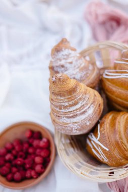 Kruvasanların yanında kırmızı böğürtlen, beyaz battaniyede çiçekler, piknik