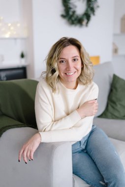 Genç bir kız beyaz bir kazakla kanepede oturuyor. Noel, yeni yıl konsepti.