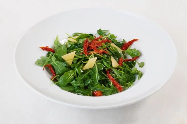 Arugula salad dried tomatoes parmesan top circular plate white background isolated — Stock Photo, Image