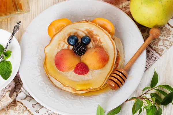 Children's breakfast pancakes smiling face of the baby teddy bear strawberry blueberry and apricot, cute food, honey — Stock Photo, Image