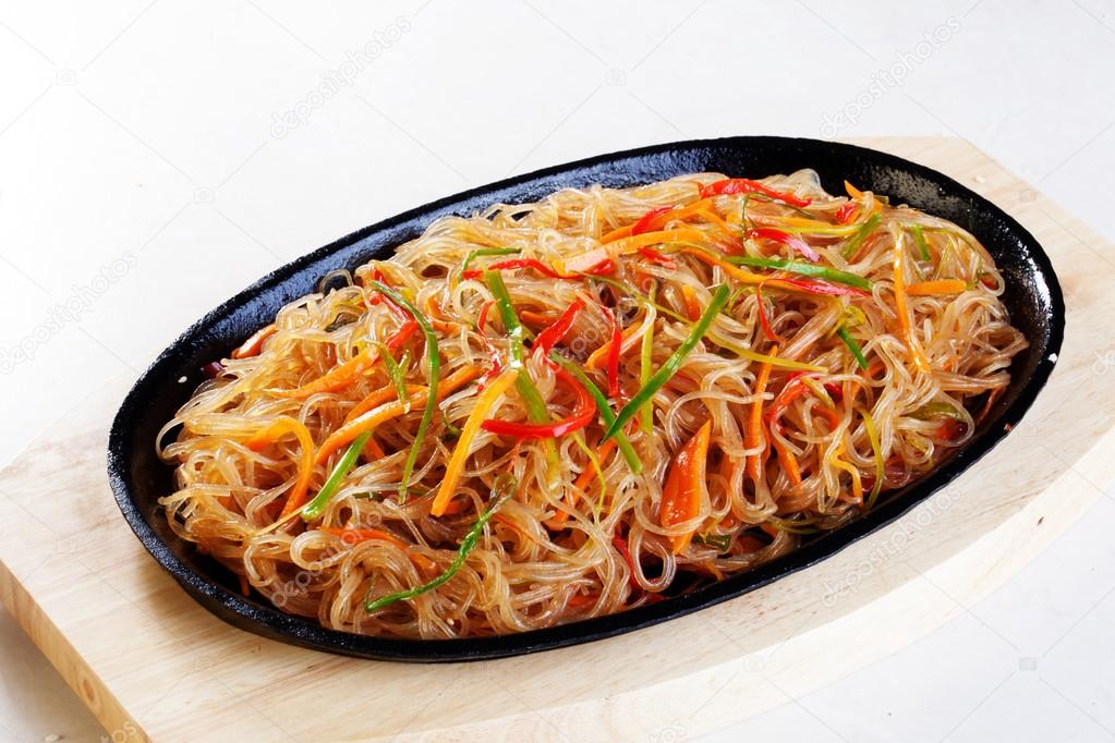 wok noodles with vegetables carrots pepper leek cast-iron frying pan on a wooden