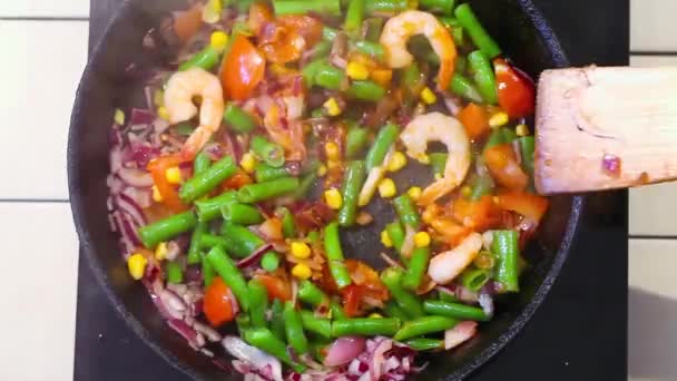 Vegetables frying pan on top, green beans, tomatoes, onions, wood, spatula, stirring  food shrimp seasoning, parsley, fennel, corn, — Stock Video