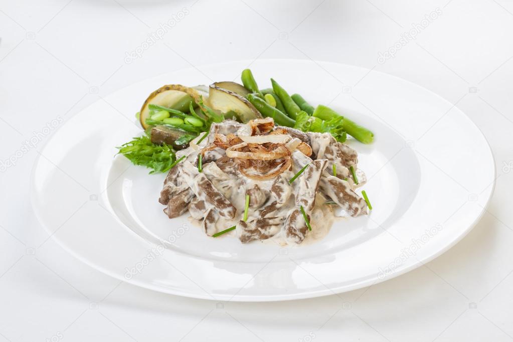 Liver Stroganoff on a plate with greens, beans and pickled cucumber      white background