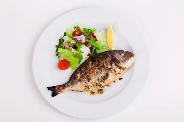 Gebackener ganzer Fisch auf einem Teller mit Gemüse und Zitrone gegrillt — Stockfoto