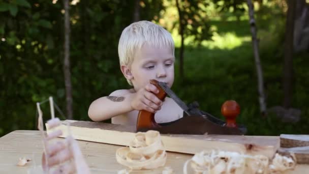 Asztalos műhely a legaranyosabb fiú gyalult fa gyalu nevetés, kék szeme, a szőke, haj Asztalos baba — Stock videók