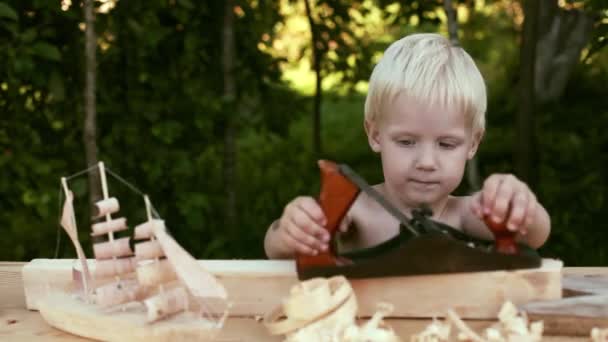 Найрідкісніший хлопчик в майстерні тесляра стругав дерев'яні плантатори сміх, блакитні очі, блондинка, волосся столярне дитя — стокове відео