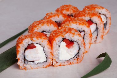 roll with tobiko orange, shrimp and sweet red peppers on a tropical leaf close-up menu isolated