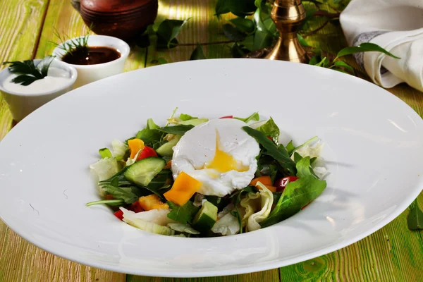 Salada com ovo escalfado, pepinos, arugula, repolho, pimentas, ainda vida em uma mesa de madeira quadro verde comida bonita — Fotografia de Stock