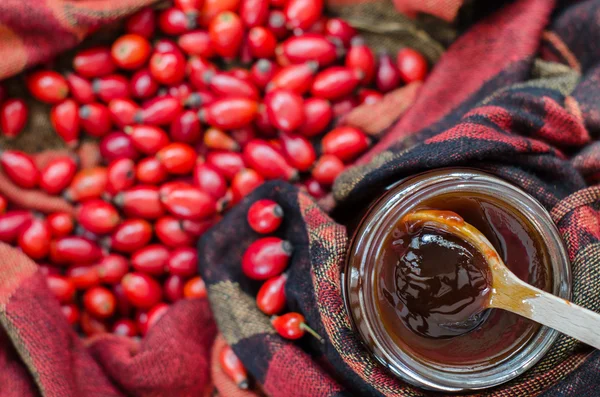 Šípkovou bobule na tkaniny terakotové barvy a lžíci s marmeládou — Stock fotografie