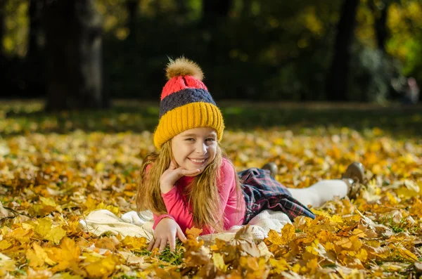 Menina muito sorridente deitado em folhas amarelas — Fotografia de Stock