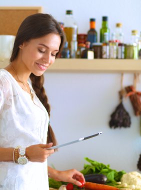 Mutfakta yemek yapmak için tablet bilgisayar kullanan genç bir kadın.