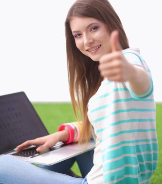 Laptoplu genç bir kadın yeşil çimlerde oturuyor.