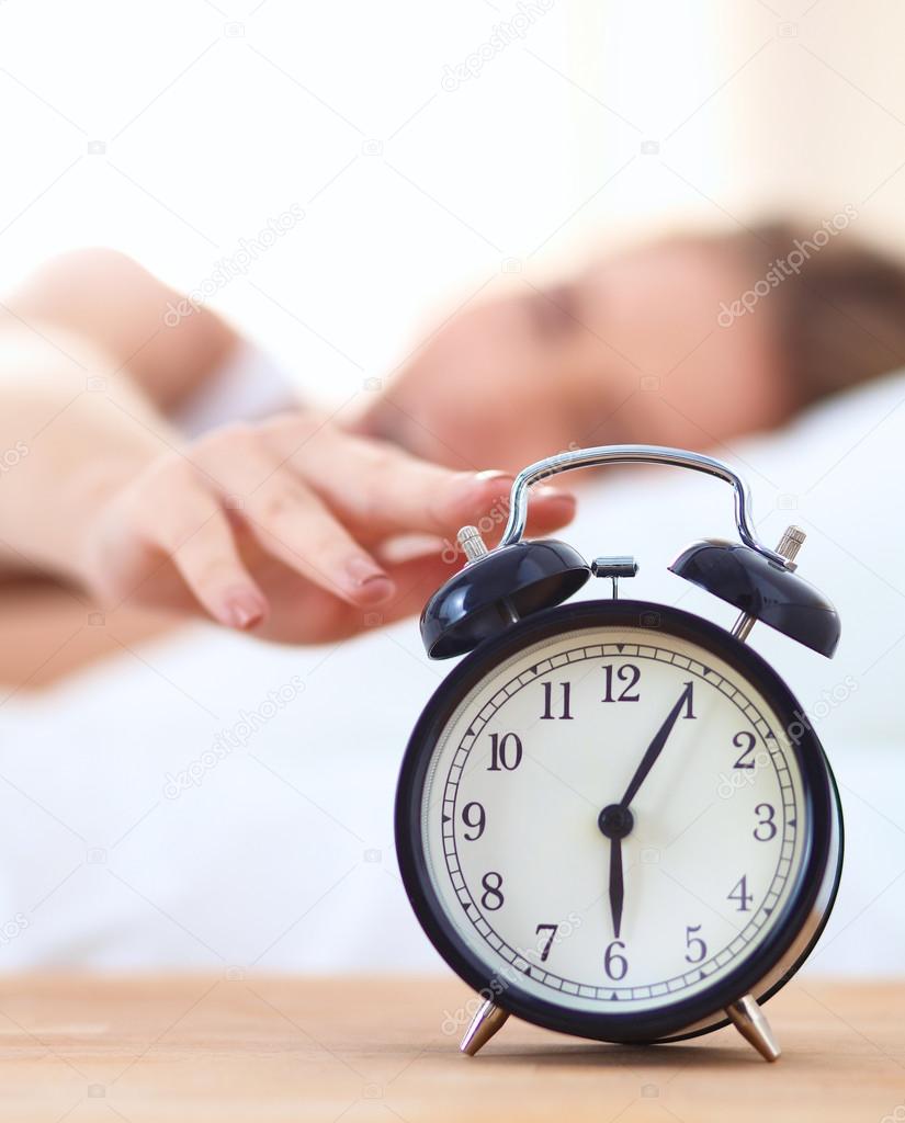 Young sleeping woman and alarm clock in bedroom at home