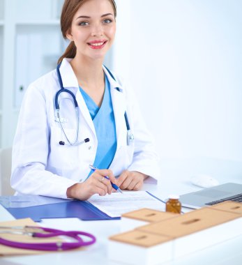 Güzel, genç, gülümseyen bayan doktor masada oturuyor ve yazıyor..