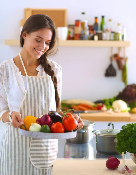 Mosolygó fiatal nő gazdaság zöldség áll a konyhában — Stock Fotó