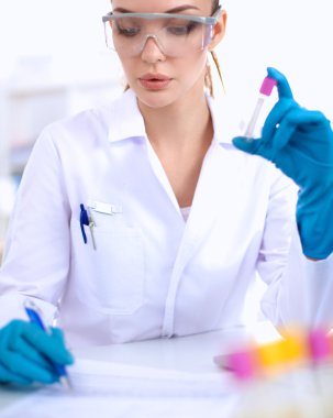 Kadın araştırmacı, beyaz arka planda izole edilmiş ilaç şişeleri ve mataralarla çevrili.