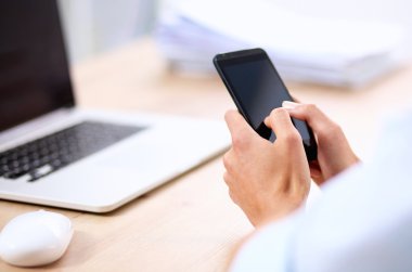 İş kadını ofiste oturan akıllı telefonuyla mesaj gönderiyor.