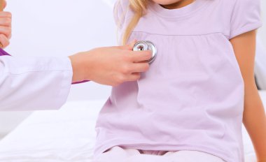 Kadın doktor ameliyatta steteskopla çocuğu muayene ediyor..