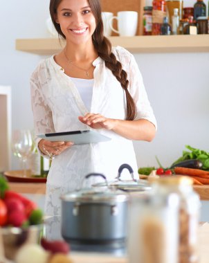 Mutfakta yemek yapmak için tablet bilgisayar kullanan genç bir kadın.