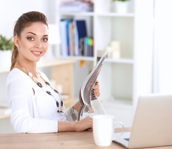 Söt affärskvinna som håller tidningen sittande vid sitt skrivbord på kontoret — Stockfoto