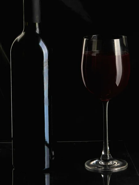 Copo de vinho elegante e uma garrafa de vinho em fundo preto — Fotografia de Stock