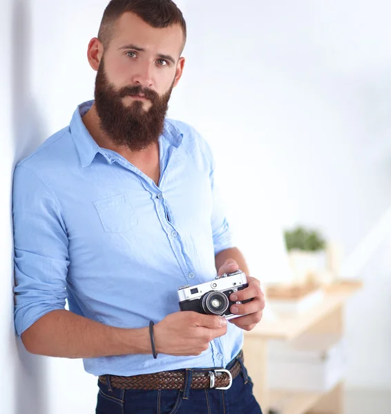 Homem barba jovem segurando uma câmera enquanto de pé contra o fundo branco — Fotografia de Stock