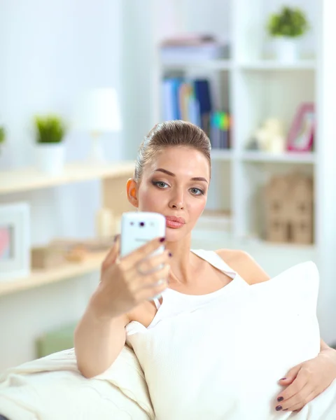 Молодая красивая женщина сидит на диване в своей комнате с помощью телефона — стоковое фото