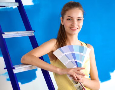 Renk paleti tutan genç, güzel bir kadın, duvarın yanında duruyor..