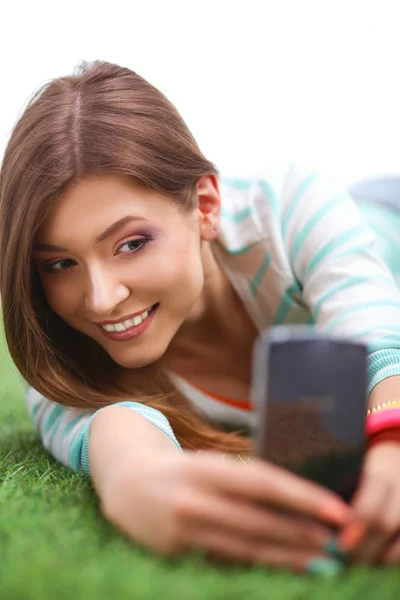 Красивая молодая женщина делает селфи по телефону, лежа в зеленой траве — стоковое фото
