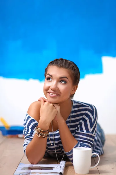 Portrait of female painter lying on floor near wall after paintingand holding a cup — Stock Photo, Image