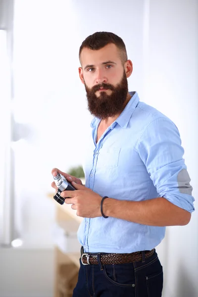 Joven barba hombre sosteniendo una cámara mientras está de pie sobre fondo blanco — Foto de Stock