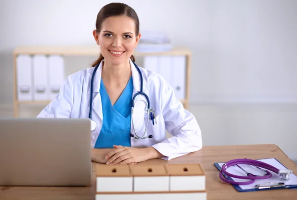 Vakker, ung, smilende kvinnelig lege som sitter ved skrivebordet og skriver:. – stockfoto