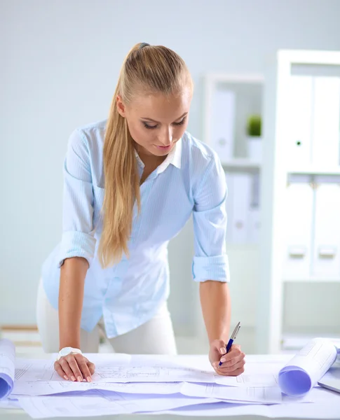 Portrait of female architect with blueprints at desk in office — Stock Photo, Image