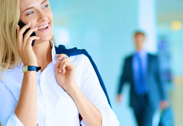 Zakenvrouw staat tegen kantoorraam te praten op mobiele telefoon — Stockfoto