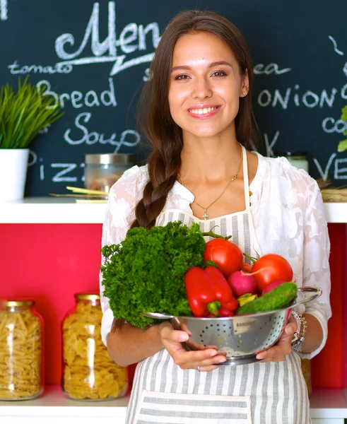 Sorridente giovane donna che tiene le verdure in piedi in cucina — Foto Stock