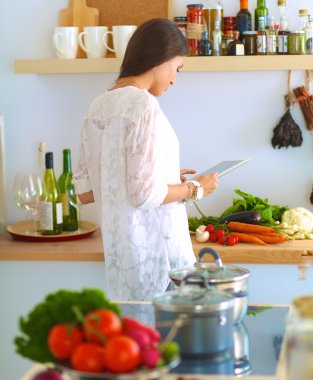 Mutfakta yemek yapmak için tablet bilgisayar kullanan genç bir kadın.