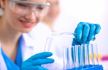 Kadın araştırmacı, beyaz arka planda izole edilmiş ilaç şişeleri ve mataralarla çevrili.