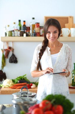 Mutfakta yemek yapmak için tablet bilgisayar kullanan genç bir kadın.