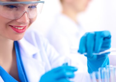 Kadın araştırmacı, beyaz arka planda izole edilmiş ilaç şişeleri ve mataralarla çevrili.