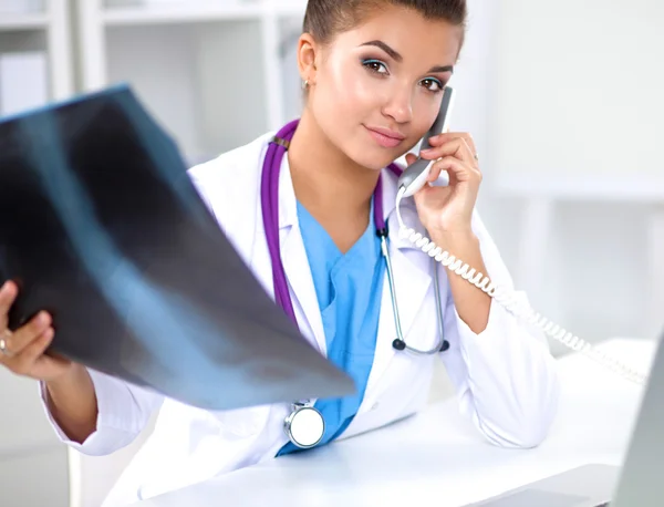 Doctora joven estudiando imagen de rayos X sentada en el escritorio —  Fotos de Stock