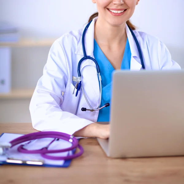 Mooie jonge glimlachende vrouwelijke arts zitten aan het bureau en schrijven. — Stockfoto