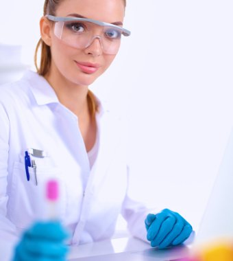 Kadın araştırmacı, beyaz arka planda izole edilmiş ilaç şişeleri ve mataralarla çevrili.