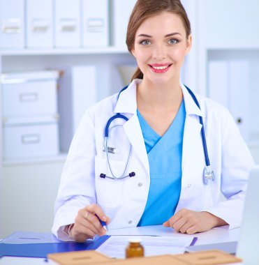 Kadın doktor masada oturuyor ve dizüstü bilgisayarla çalışıyor.